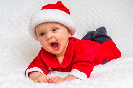 Cute newborn baby with Santa costume yawning and lying on white blanketの写真素材