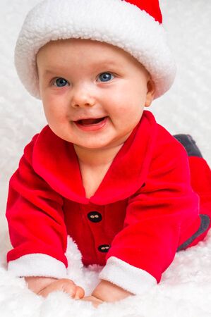 Happy smiling baby lying on white blanket with santa hat and suitの写真素材