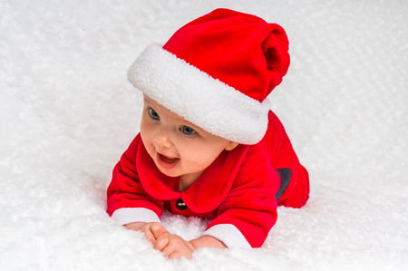 Happy smiling baby lying on white blanket with santa hat and suitの写真素材