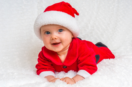 Funny Christmas baby in Santa Claus costume lying on white blanketの写真素材