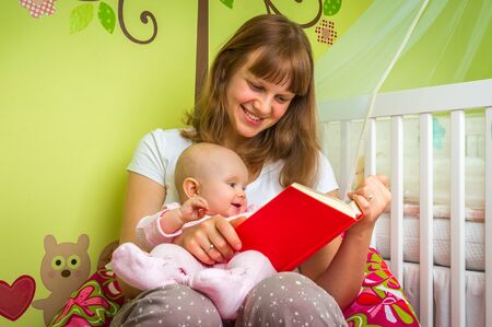 Happy mother reading a book to her baby girl at homeの写真素材