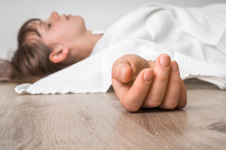 Dead woman lying on the floor under white cloth with focus on handの写真素材