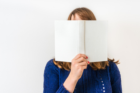Pretty woman reading a book and covering her face isolated on whiteの写真素材