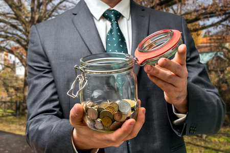 Businessman in black suit holding money jar with coins on the street