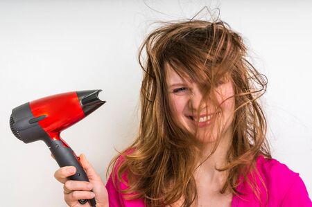 Beautiful young woman dries hair with red hair dryerの写真素材