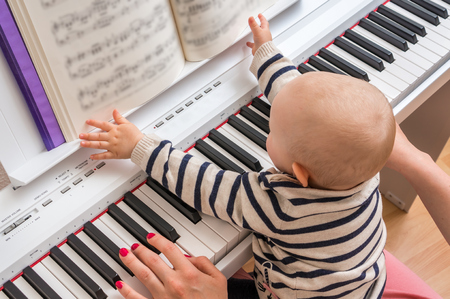 Mother teaching her cute baby to play piano at homeの写真素材