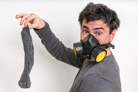 Man with gas mask is holding stinky sock - unpleasant smell conceptの写真素材