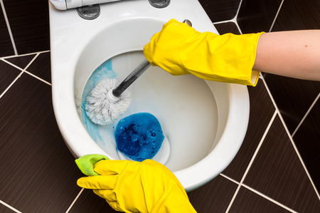 Woman in yellow rubber gloves is cleaning toilet bowl using brushの写真素材