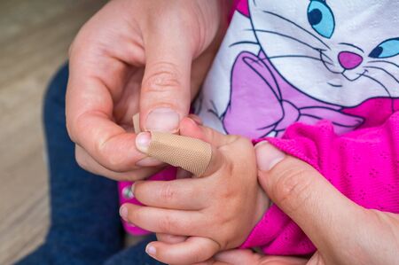 Mother applying plaster around finger of little girlの写真素材
