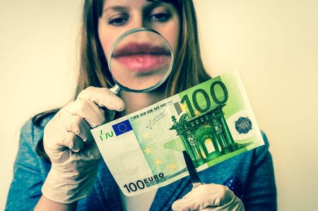 Woman viewing counterfeit euro banknote with magnifying glass - retro style