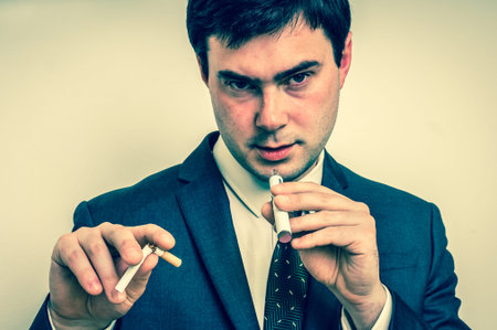 Businessman in suit is comparing electronic cigarette and tobacco cigarette - retro styleの写真素材