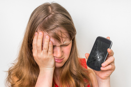 Sad woman is holding mobile phone in her hand with broken screenの写真素材