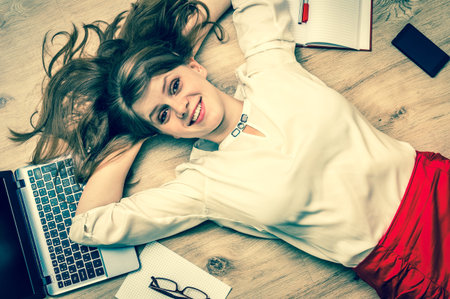 Smiling woman lying on back with laptop and smartphone - study and education concept - retro styleの写真素材