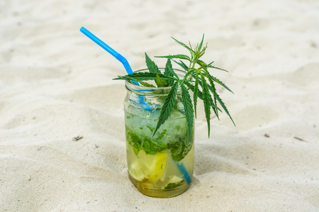 Mojito drink with leafs of marijuana plant on sandの写真素材