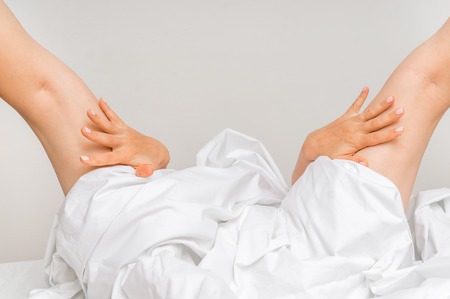 Attractive sexy woman with spreaded legs on bed covering with a blanketの写真素材