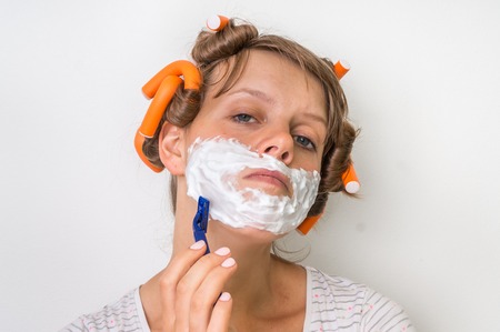Attractive young woman shaves her face with foam and razorの写真素材