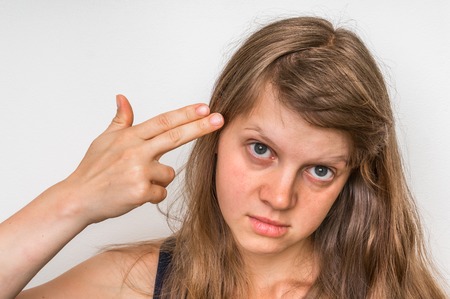 Woman committing suicide with two fingers - headshot portrait of depressed womanの写真素材