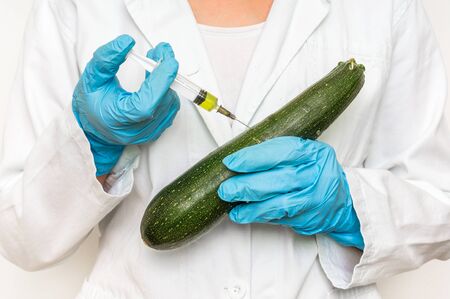 GMO scientist injecting liquid from syringe into zucchini - genetically modified food conceptの写真素材