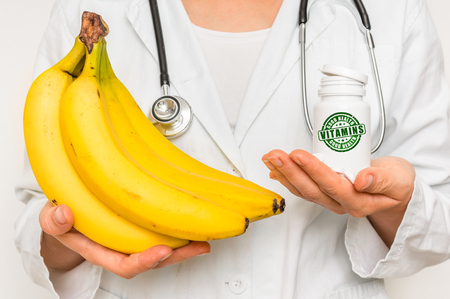 Female doctor compare pile of pills with fresh banana - healthy food conceptの写真素材