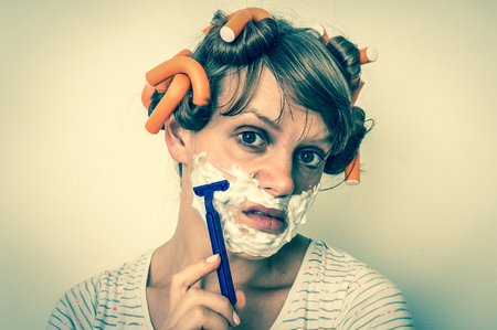 Attractive young woman shaves her face with foam and razor - retro styleの写真素材