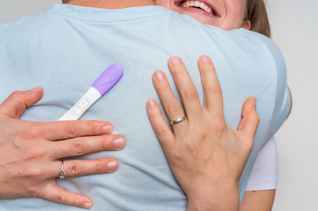 Happy pregnant woman with positive pregnancy test hugging her husbandの写真素材