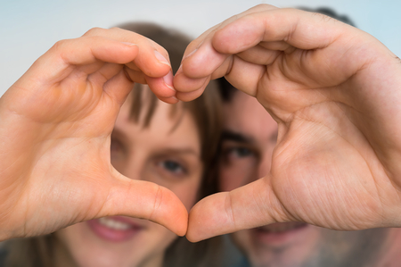 Couple making heart shape with hands and looking through it - loving couple conceptの写真素材