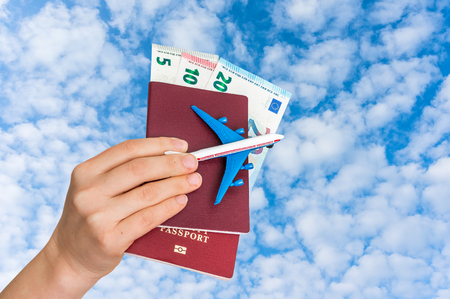 Airplane, passport and money in female hand on blue sky background - travelling conceptの写真素材