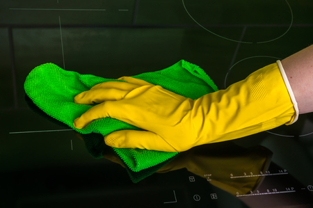Hand in glove with green rag is wiping induction plates - housework and housekeeping conceptの写真素材