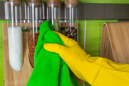 Hand in glove with green rag is wiping spice bottles - housework and housekeeping conceptの写真素材