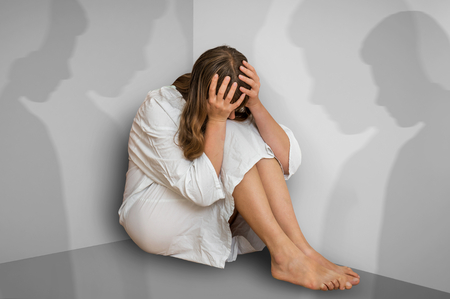 Scared woman with schizophrenia sitting in the corner at room with people shadows - hallucinations and schizophrenia disease conceptの写真素材