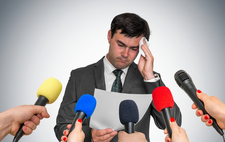 Nervous man is sweating, he afraid of public speech. Many microphones around.の写真素材