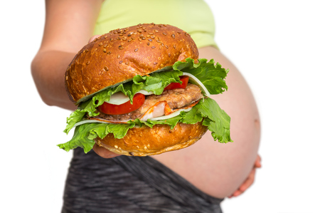 Pregnant woman with belly is holding a burger - unhealthy eating in pregnancy conceptの写真素材