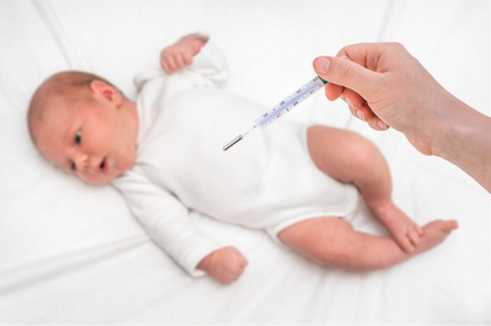 Measuring temperature to a newborn baby with mercury thermometer - cold and flu conceptの写真素材