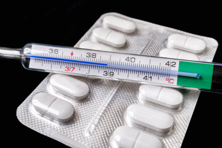 Close-up of mercury thermometer with pills on background - fever concept