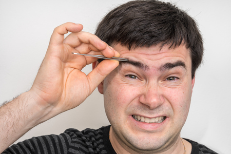 Young man is plucking eyebrows with tweezersの写真素材