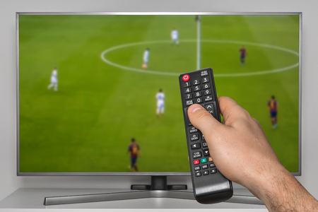 Football match on TV and human hand with TV remote controllerの写真素材