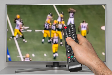 Rugby match on TV and human hand with TV remote controllerの写真素材