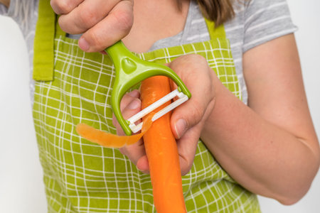 Woman peeling a carrot using food peeler 
- vegetables food cooking concept