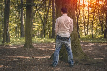 Standing man peeing near big tree in autumn forest in nature - incontinence conceptの写真素材