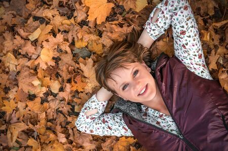 Attractive woman is lying over autumn leaves in park and smiling, top viewの写真素材