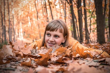 Attractive woman is lying over autumn leaves in park and smiling, top viewの写真素材