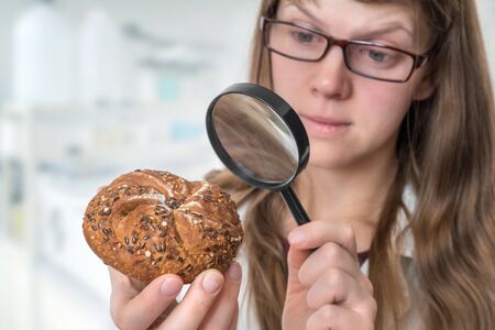 Scientist examines a kaiser bun with magnifying glass - unhealthy dangerous ingredients in foodsの写真素材