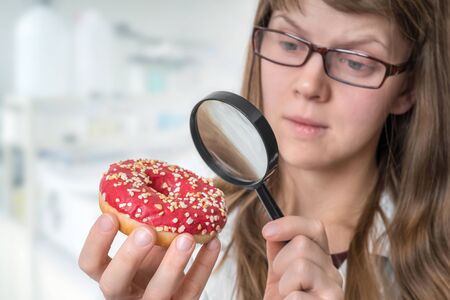 Scientist examines a donut with magnifying glass - unhealthy dangerous ingredients in foodsの写真素材