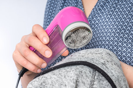 Woman is removing lint with fabric shaver or fuzz remover - clothes care conceptの写真素材