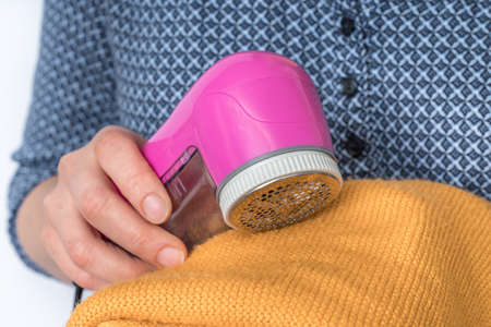 Woman is removing lint with fabric shaver or fuzz remover - clothes care conceptの写真素材