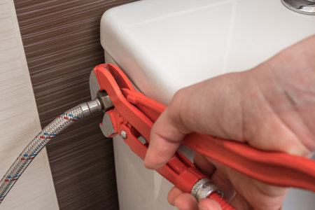 Plumber is repairing toilet cistern using a wrenchの写真素材