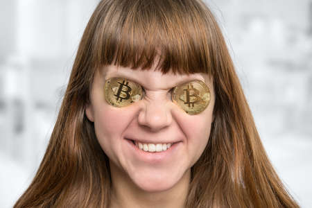 Smiling woman with bitcoin coins in front of her eyesの写真素材