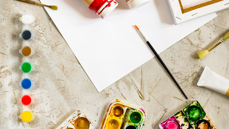 Flatlay with bright paints in small round containers and many palettes, brush and white sheet of paper on grey cement backcground, Workspace, Mess, drawing, Hobby, Art Horizontal banner creativeの写真素材