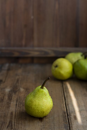 one fresh ripe organic yellow pear on rustic wooden brown table with defocused pears on background. Selective focus. Vertical with copy space. For design about agricilture, fruit and healthy foodの写真素材