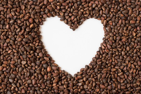 Brown fresh natural whole pine nuts, seeds of Siberian pine. Empty heart shape white space in the middle. Horizontal orientation. Copy space.の写真素材